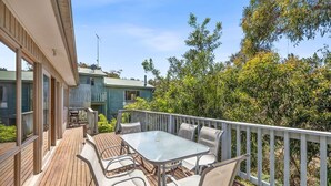 A wooden deck with a table and chairs, surrounded by a white railing, overlooking a garden and a house. - Oasis on Weir (Anglesea)