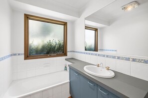 Ein Badezimmer mit Badewanne, Waschbecken und einem Fenster mit Blick auf Grünflächen.