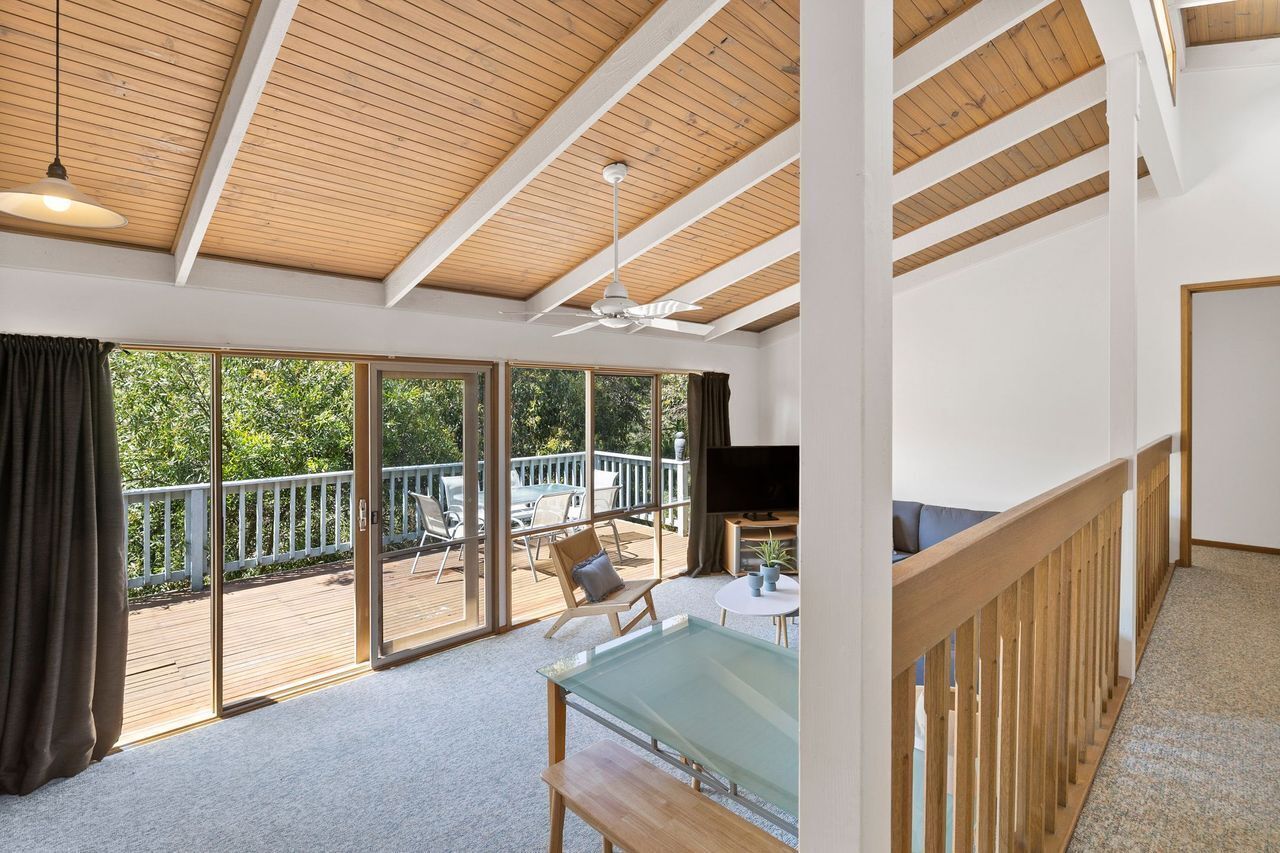 A spacious room with a large sliding glass door leading to a deck, a ceiling fan, and a television.