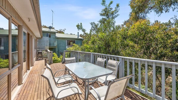 Une terrasse avec une table et des chaises, entourée d’une autre terrasse en bois et d’une balustrade blanche.