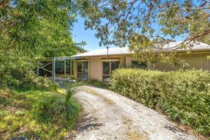 A house with a gravel driveway, surrounded by dense greenery and trees. - Oasis on Weir (Anglesea)