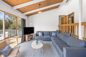 A modern living room with a sectional sofa, a flat-screen TV, a small round table, and a balcony with outdoor seating. - Oasis on Weir (Anglesea)