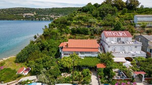 Un edificio costero con techo rojo, rodeado de vegetación exuberante y vistas al mar.