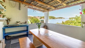 Terraza costera con una mesa de madera, un banco azul y plantas en macetas.
