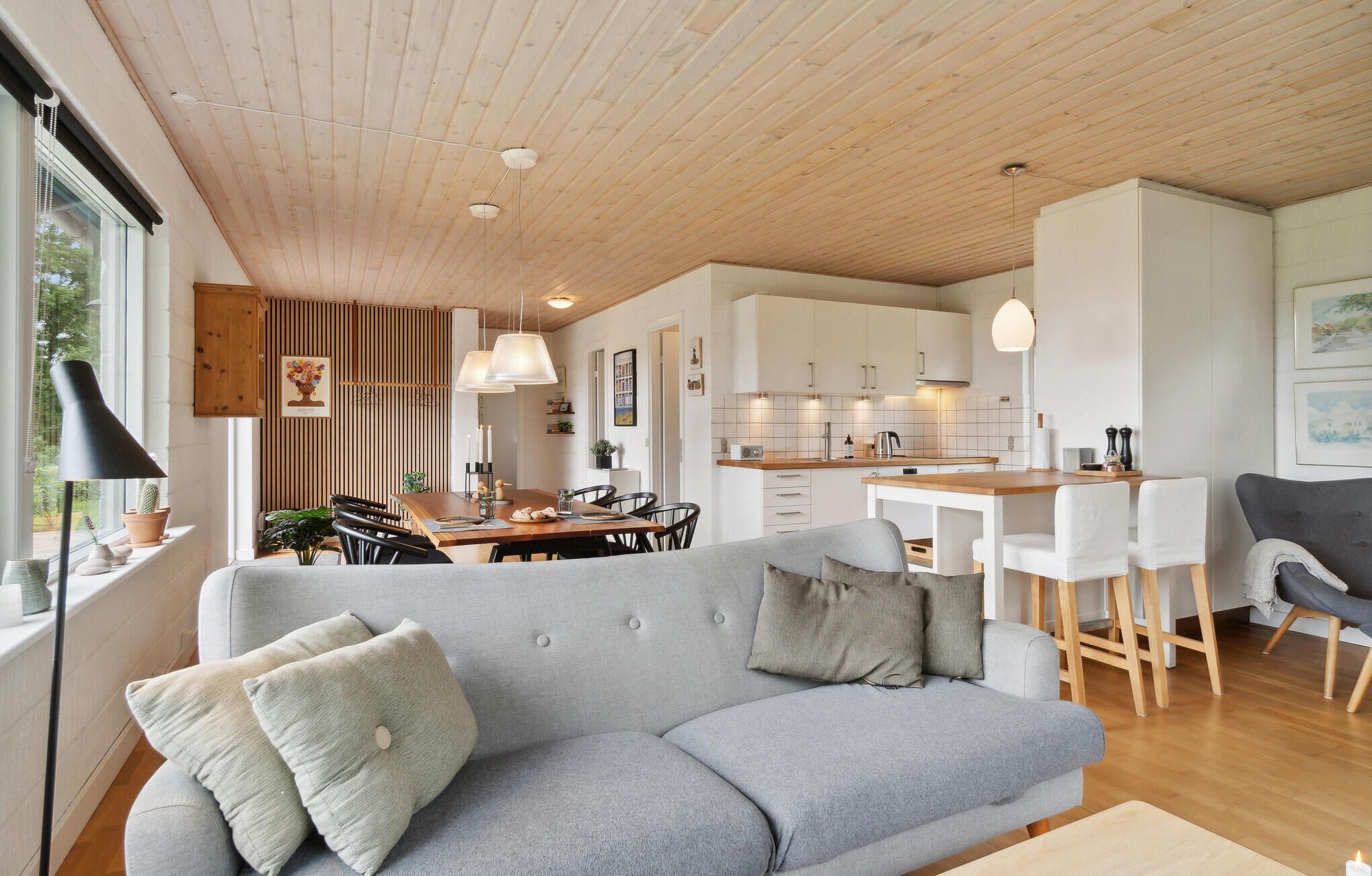 En moderne stue med en grå sofa, træloft og et køkken med hvide skabe og en træbordplade.
