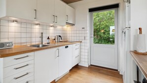A modern kitchen with white cabinets, a wooden countertop, and a view of greenery outside. - Lovely home in Samsø with WiFi (Samsø)