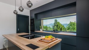 A modern kitchen with a central island, a built-in oven, and a large window offering a scenic view. - Gorgeous home in Nedescina with sauna (Nedescina)