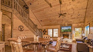 A log cabin interior with a wooden dining table, chairs, a fireplace, a sofa, and a staircase. - 🏔️A Wild Mountain Splash: Mtn View, Pets, Secluded, Theater, Games, Hot Tub (Sevierville)