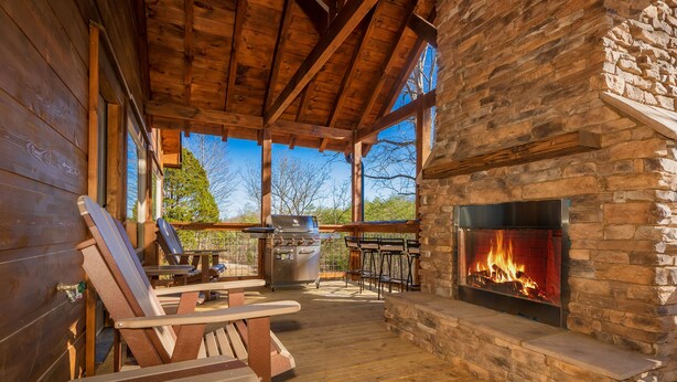 A wooden deck with Adirondack chairs, a stone fireplace, and a grill area. - 🏔️A Wild Mountain Splash: Mtn View, Pets, Secluded, Theater, Games, Hot Tub (Sevierville)