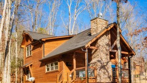 A wooden cabin with a stone chimney, wooden deck, and a staircase leading to the entrance. - 🏔️A Wild Mountain Splash: Mtn View, Pets, Secluded, Theater, Games, Hot Tub (Sevierville)