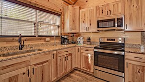 A kitchen with wooden cabinets, a granite countertop, a stainless steel sink, a microwave, and an oven. - 🏔️A Wild Mountain Splash: Mtn View, Pets, Secluded, Theater, Games, Hot Tub (Sevierville)