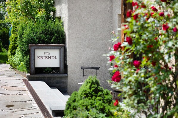 A sign with 'Villa KRIENDL' on a building facade, surrounded by greenery and a stone pathway.