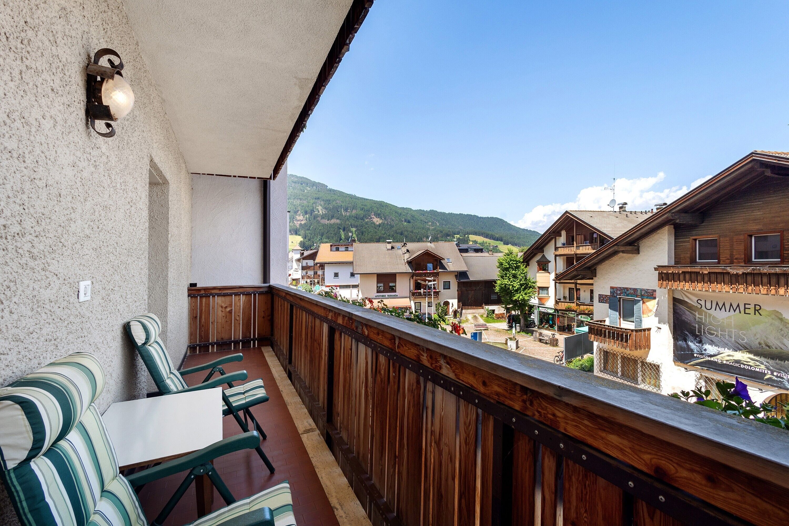 Een balkon met houten spijlen, een tafel en stoelen, met uitzicht op een dorp met huizen en een berg op de achtergrond.