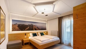 Un dormitorio moderno con una cama grande, cabecero de madera, una obra de arte en la pared que representa un paisaje montañoso, una mesita de noche y un banco.