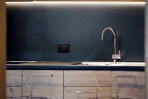 A kitchen with a modern faucet, wooden cabinets, and a dark backsplash.