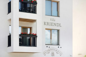 A multi-story building with balconies, a sign reading 'Villa KRIENDL,' and a logo for 'Prodevilla Spa Textiles.'
