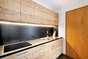 A modern kitchen with wooden cabinetry, a black countertop, and a stainless steel sink.