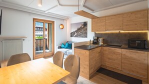 Een moderne keuken met houten kasten, een inbouwmagnetron en een eethoek met een houten tafel en stoelen.