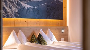 Een hotelkamer met een houten hoofdeinde, wit beddengoed en uitzicht op de bergen.