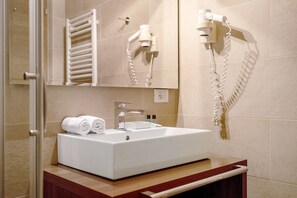 Ein Badezimmer mit weißem Waschbecken, Handtuchspender und einem an der Wand montierten Fön.