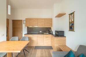 Een compacte keuken met houten kastjes, een ingebouwde magnetron, en een klein eetgedeelte met een tafel en stoelen.