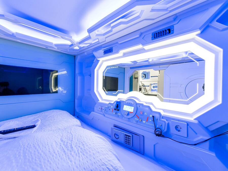 A futuristic room with a bed, a control panel, and a large mirror.