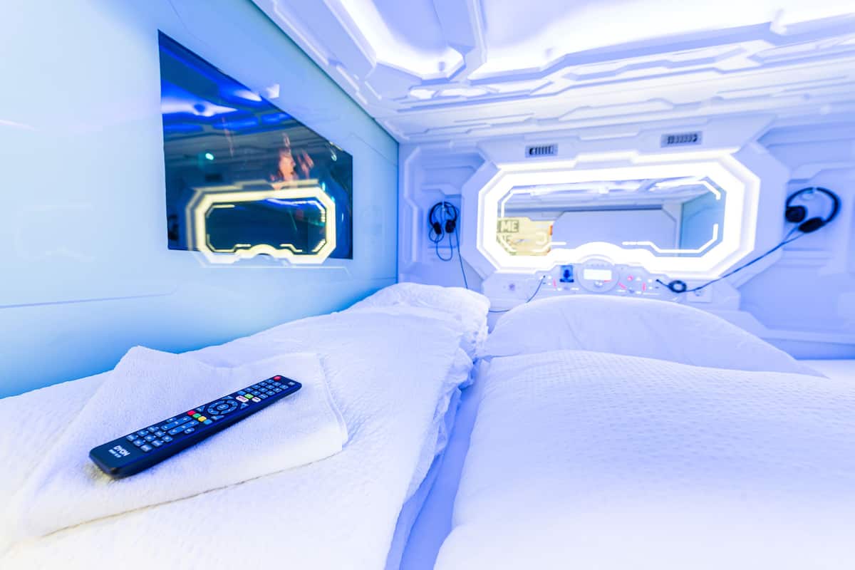 A modern room with a bed, a remote control, and a mirror.