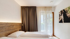 Ein Schlafzimmer mit einem hölzernen Kopfteil, einem Bett mit weißer Bettwäsche, einem Fenster mit transparenten Vorhängen und einem Wandbild.