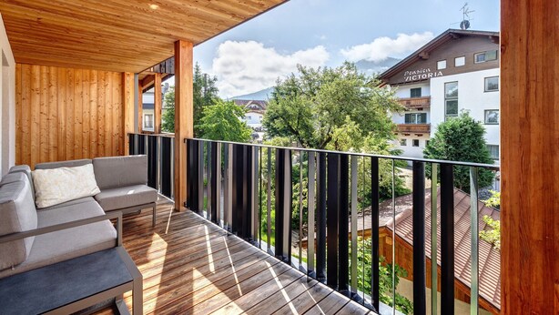 Ein Holzbalkon mit einer Couch, Blick auf Gebäude und einem klaren Himmel.