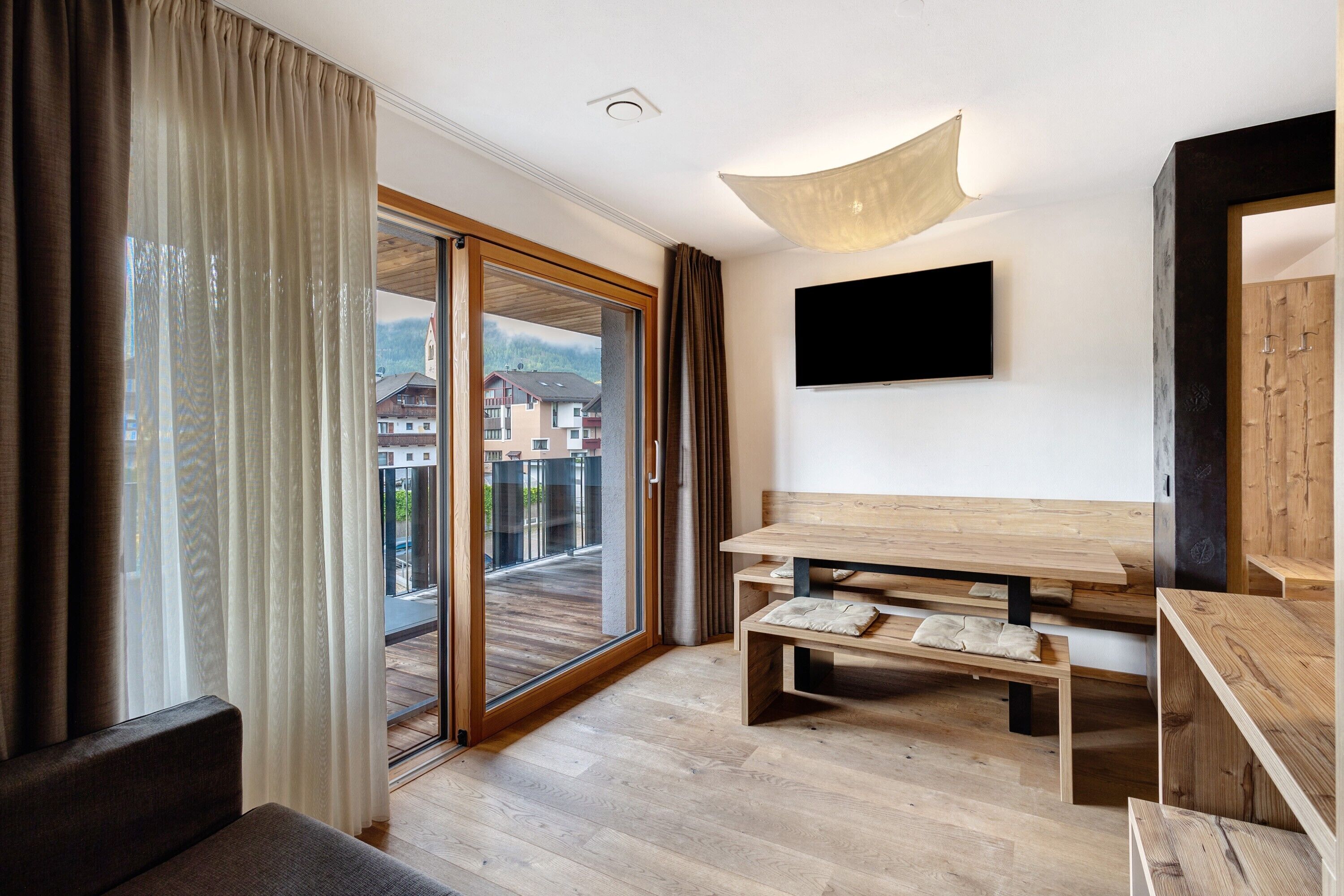 Quarto moderno com piso de madeira, um sofá, uma mesa e TV fixada na parede.