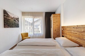 Une chambre d’hôtel avec deux lits, une armoire en bois, une chaise et une grande fenêtre avec des rideaux.