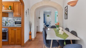A dining area with a white table, grey chairs, and a white rabbit statue. There is a kitchen with wooden cabinets and a tiled backsplash.