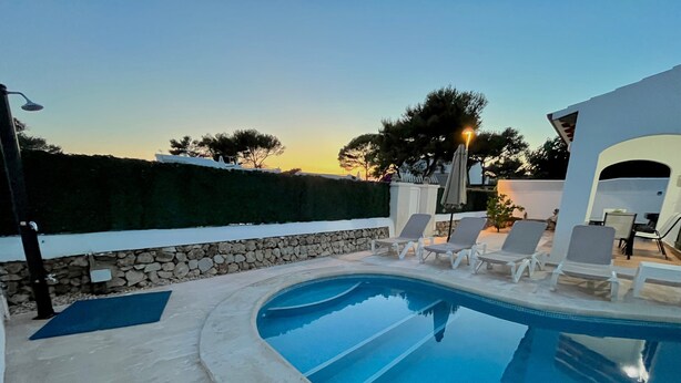 A swimming pool with lounge chairs, a stone wall, and a hedge.