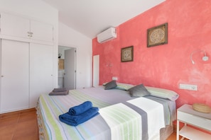 A bedroom with a bed, a wardrobe, an air conditioner, and a bedside table.