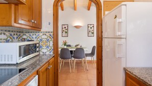 A kitchen with wooden cabinets, a white refrigerator, a microwave, and a dining area with chairs and a table.