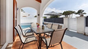An outdoor patio with a table and chairs, a pool, and a view of the sea.