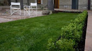 A well-maintained lawn with two white folding chairs and a stone building with a stone facade and a metal gate in the background. - Benozzo vacation apartment with garden and pool (Montefalco)
