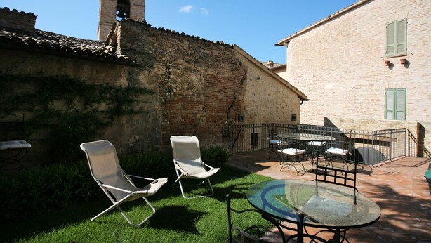 A courtyard with a stone wall, a bell tower, and a glass table with chairs. - Benozzo vacation apartment with garden and pool (Montefalco)