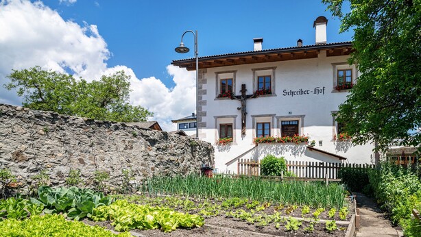 Un edificio con un muro de piedra, un jardín con diversas hortalizas y una valla de madera.