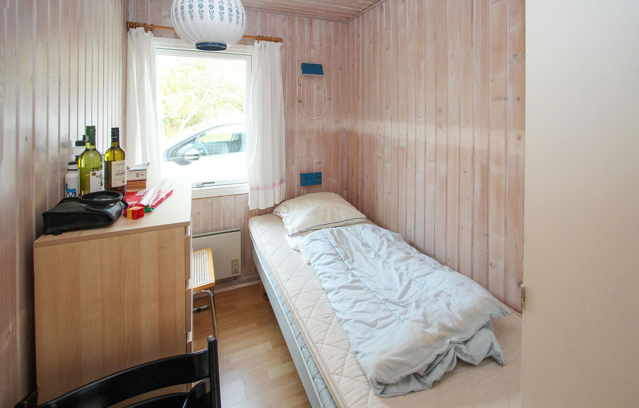 Una habitación pequeña con cama individual, un escritorio de madera, una silla y una ventana con cortinas.