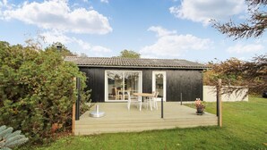 A small wooden building with a tiled roof, a glass door, and a patio with outdoor furniture.