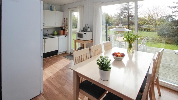 A modern kitchen with white cabinets, a dining table with chairs, and a view of the garden through large windows.