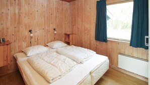 A wooden-paneled room with a bed, two bedside tables, a window with curtains, and a radiator.