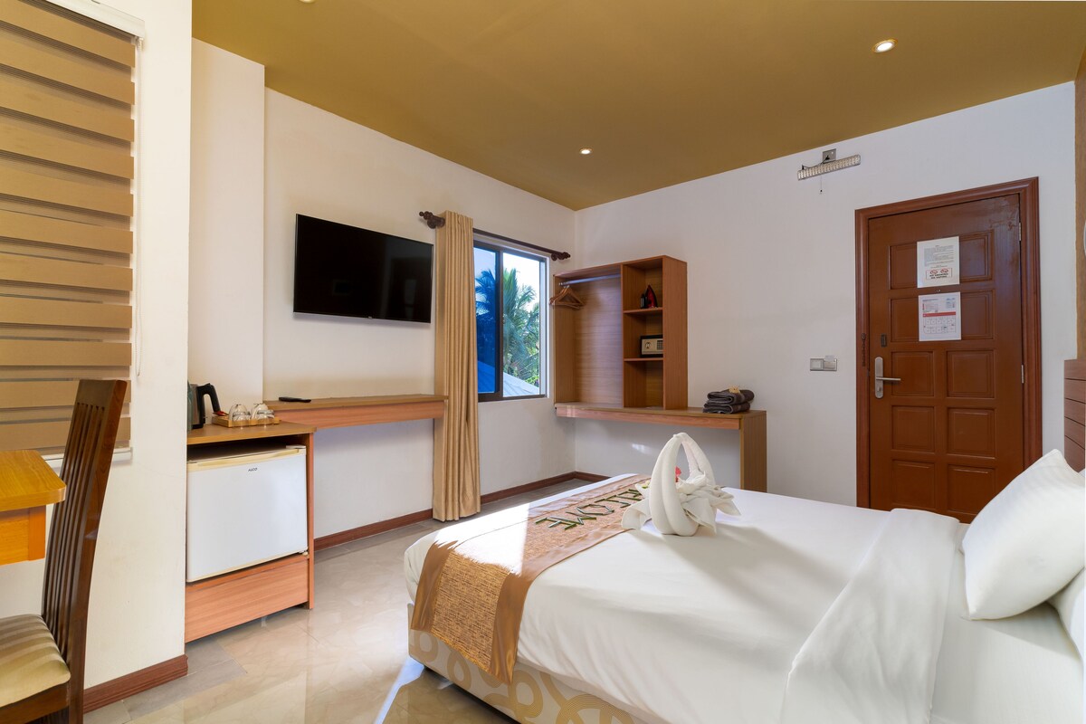 A hotel room with a bed, a desk, a television, a wardrobe, and a door.