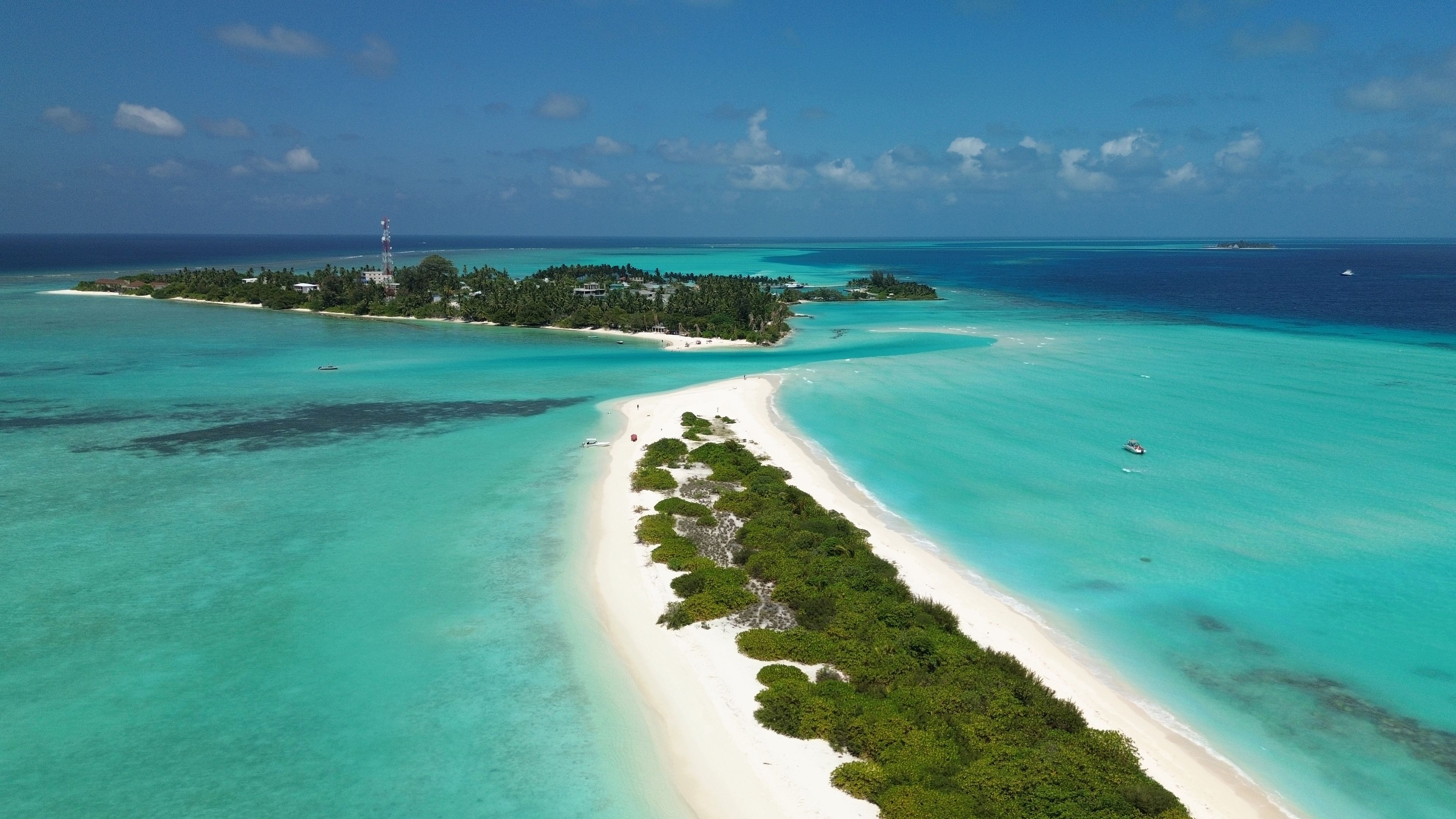 Vista aérea de una isla tropical con una playa de arena blanca, aguas turquesas cristalinas y exuberante vegetación.