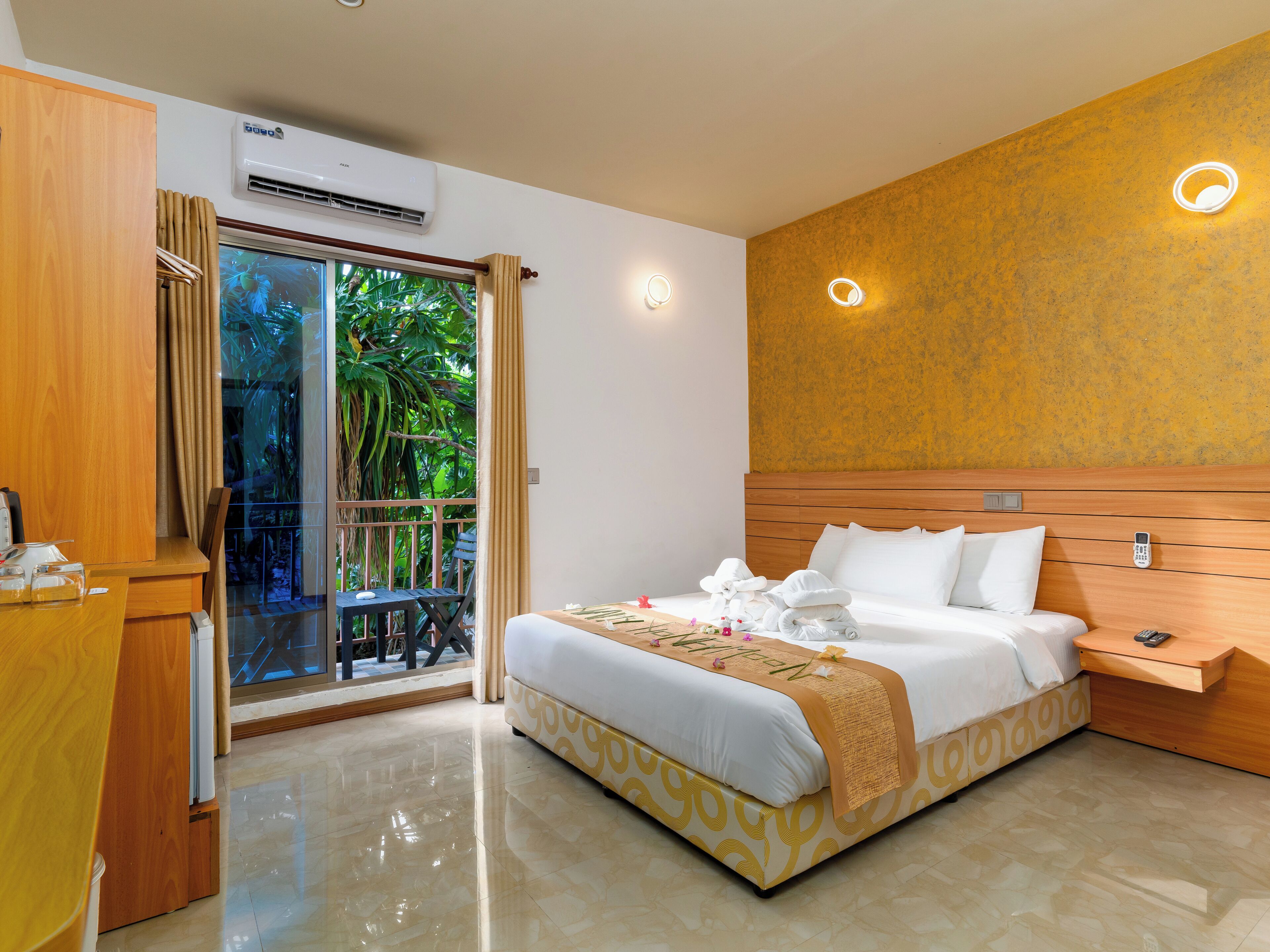 Habitación de hotel con cama, mesita de noche y vista a la vegetación a través de una puerta corredera.