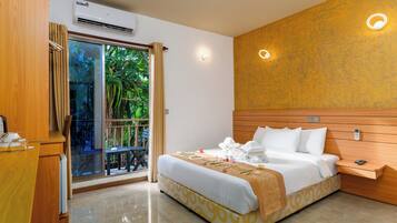 Habitación de hotel con cama, mesita de noche y vista a la vegetación a través de una puerta corredera.