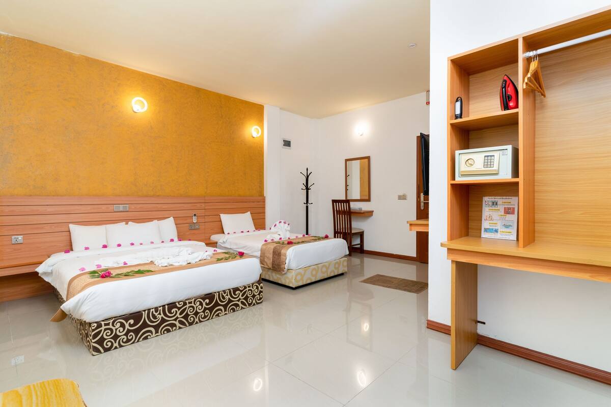Habitación de hotel con dos camas, cabecero de madera, mesita de noche, espejo, perchero y estante con una radio y un folleto.