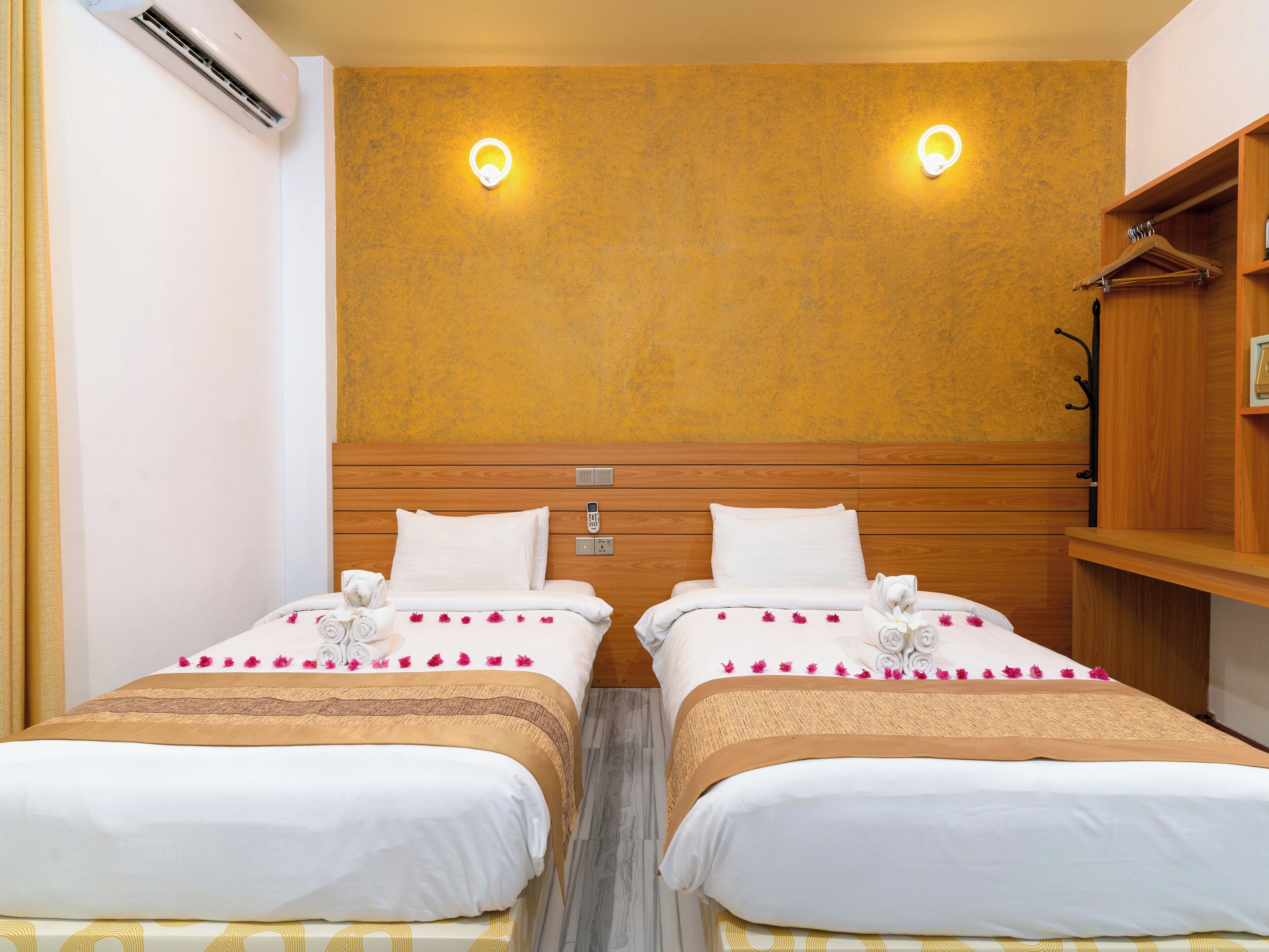 Habitació d'hotel amb dos llits, un panell de capçalera de fusta, aire condicionat fixat a la paret i un armari de fusta.