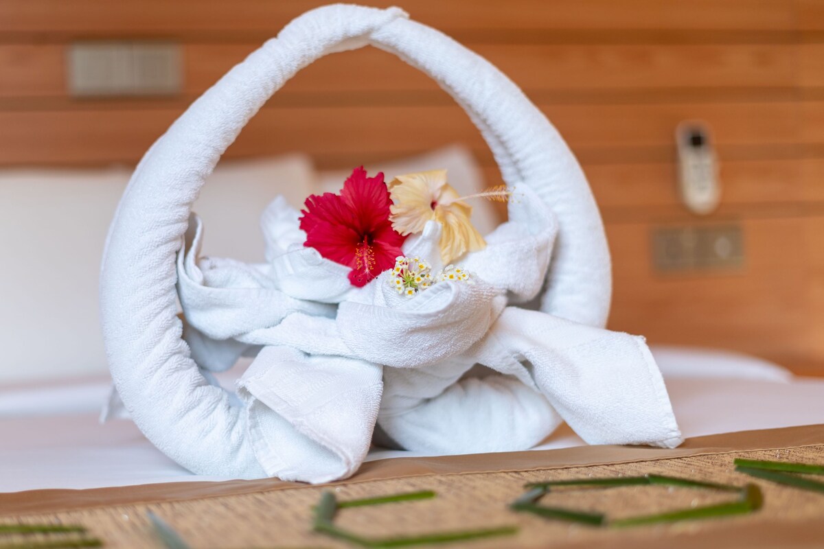 Ein ordentlich drapiertes Handtuch mit einem weißen Handtuchhalter, einer roten Hibiskusblüte und einer gelben Blüte, platziert auf einer Holzfläche.